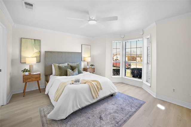 bedroom with baseboards, light wood finished floors, visible vents, and crown molding