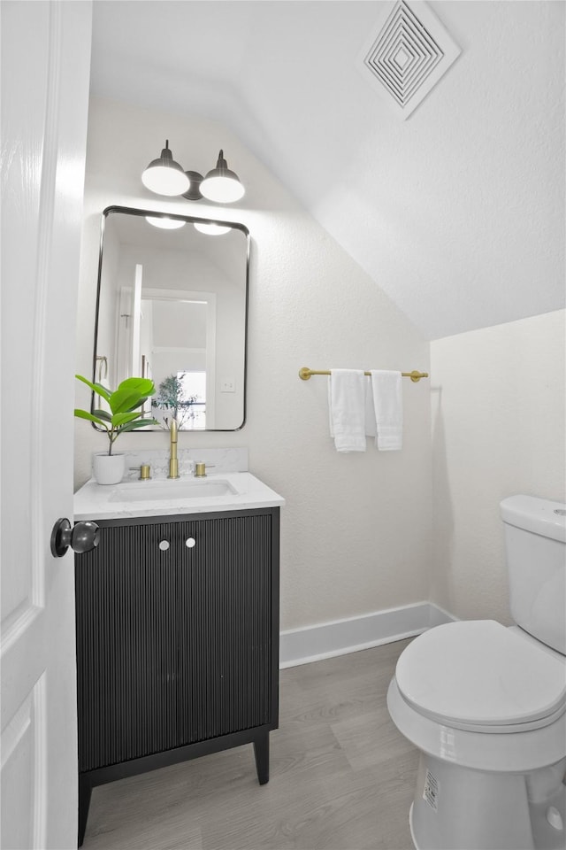 half bath with lofted ceiling, visible vents, toilet, vanity, and baseboards