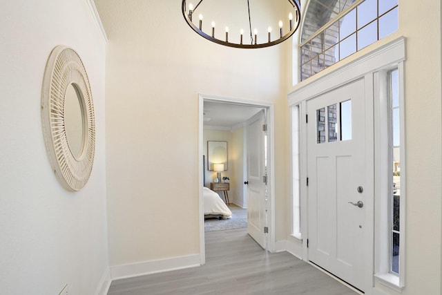 entryway with baseboards, light wood-style flooring, an inviting chandelier, a high ceiling, and crown molding