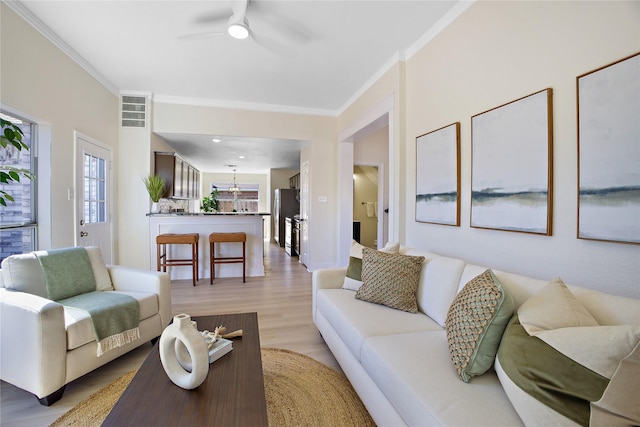 living room featuring light wood-style flooring, visible vents, ornamental molding, and ceiling fan