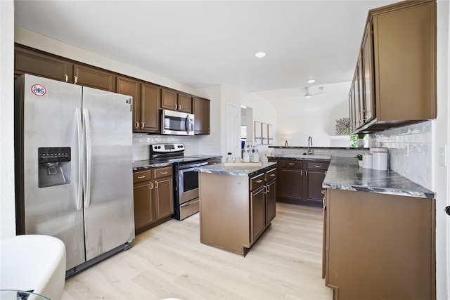 kitchen featuring stainless steel appliances, a center island, light wood-style flooring, and a peninsula