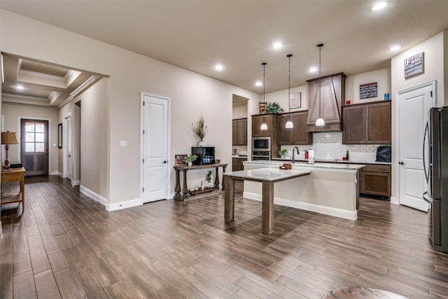 kitchen with custom exhaust hood, dark wood-style floors, appliances with stainless steel finishes, and an island with sink