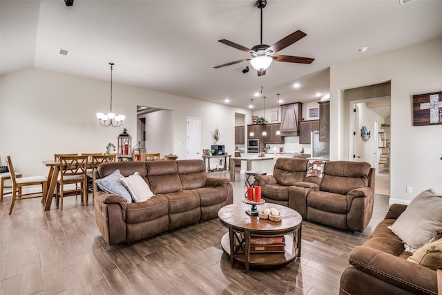 living area featuring visible vents, ceiling fan with notable chandelier, lofted ceiling, and wood finished floors