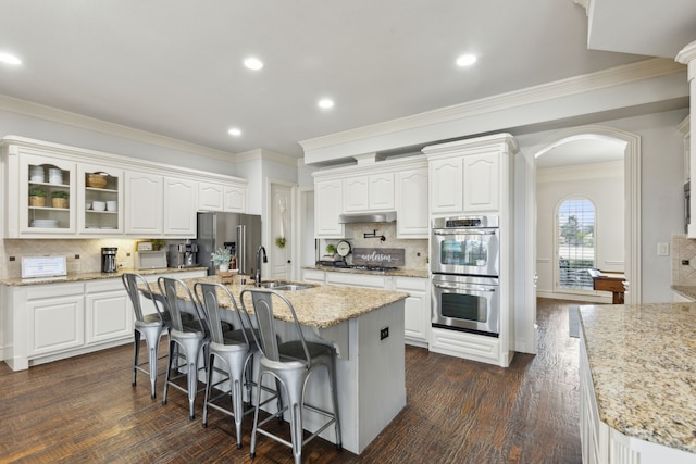 kitchen with a breakfast bar area, appliances with stainless steel finishes, arched walkways, white cabinets, and a sink