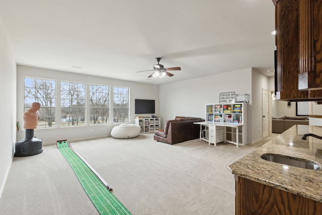 carpeted living area featuring a sink, baseboards, and a ceiling fan