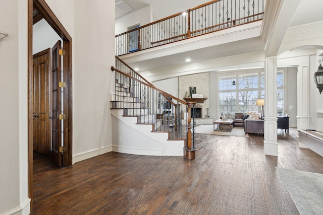 entryway with decorative columns, a fireplace, wood finished floors, and a towering ceiling