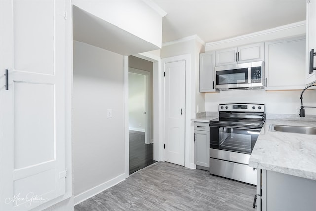kitchen with stainless steel appliances, a sink, baseboards, ornamental molding, and light wood finished floors
