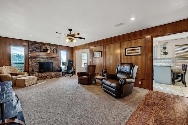 living area with a wealth of natural light, wood walls, a brick fireplace, and visible vents