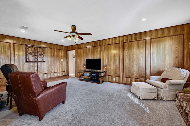 carpeted living room with a ceiling fan, recessed lighting, visible vents, and wooden walls