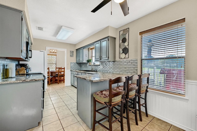 kitchen with light tile patterned floors, a peninsula, visible vents, wainscoting, and gray cabinets