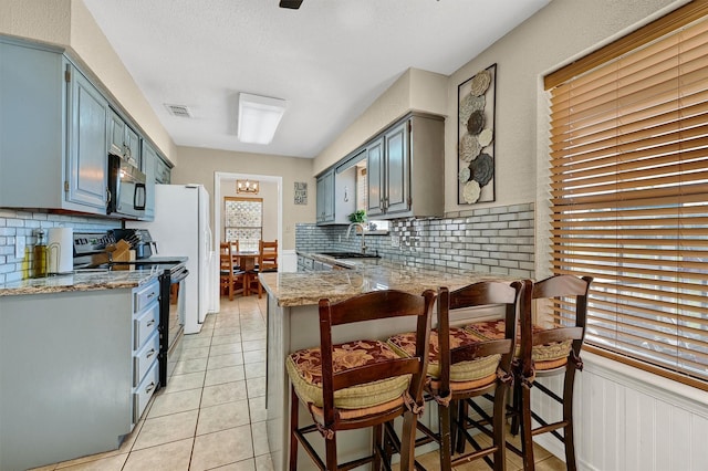 kitchen featuring light tile patterned floors, a peninsula, electric range, a sink, and stainless steel microwave