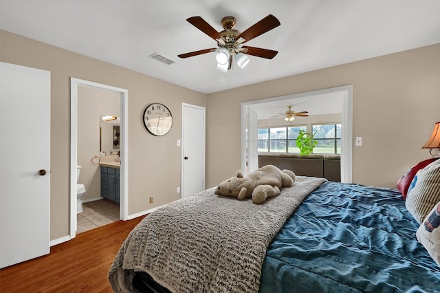 bedroom with visible vents, a ceiling fan, ensuite bath, wood finished floors, and baseboards