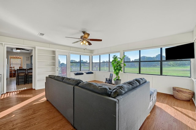 living area featuring a ceiling fan, visible vents, built in shelves, and wood finished floors