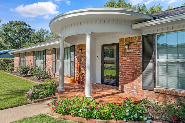 property entrance featuring covered porch, brick siding, and a lawn