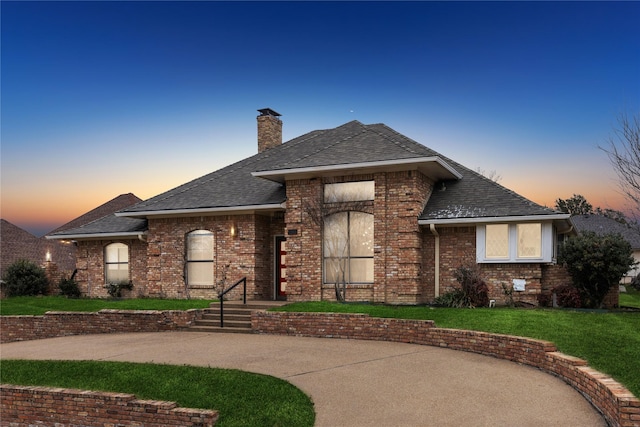 view of front of house with roof with shingles, a chimney, a lawn, and brick siding