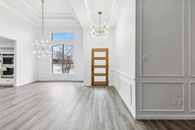 foyer featuring light wood finished floors, a decorative wall, and a notable chandelier