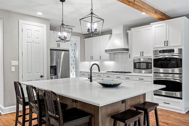 kitchen with a kitchen island with sink, stainless steel appliances, a breakfast bar, light countertops, and custom range hood