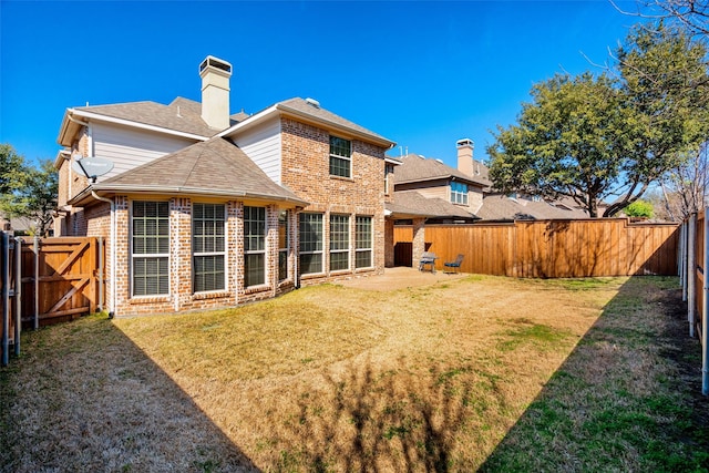 rear view of property with a yard, brick siding, a chimney, and a fenced backyard