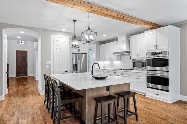 kitchen with white cabinets, an island with sink, appliances with stainless steel finishes, light countertops, and premium range hood