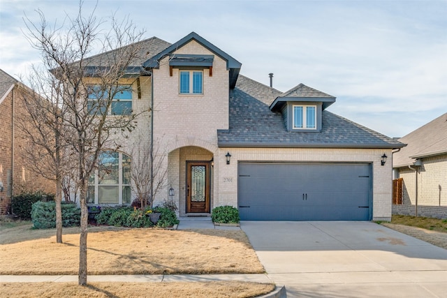 view of front of property featuring a garage, driveway, brick siding, and roof with shingles