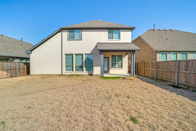 rear view of property with a patio, a fenced backyard, roof with shingles, a yard, and brick siding