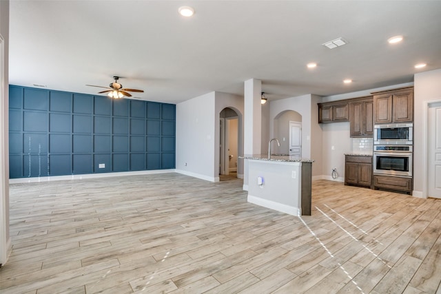 kitchen with light stone counters, arched walkways, stainless steel microwave, open floor plan, and ceiling fan