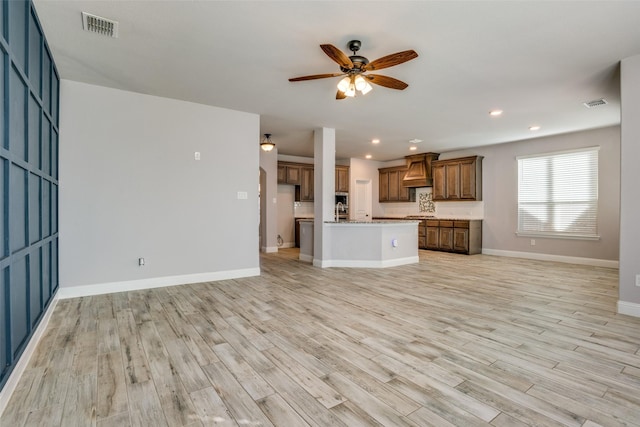 unfurnished living room featuring light wood-type flooring, ceiling fan, visible vents, and baseboards