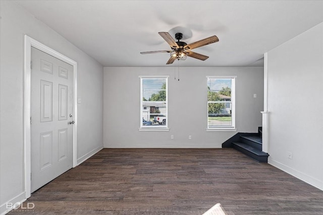 unfurnished living room featuring stairway, baseboards, a ceiling fan, and dark wood-style flooring