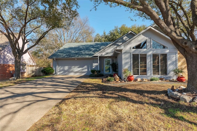 view of front facade with a shingled roof, concrete driveway, fence, and an attached garage