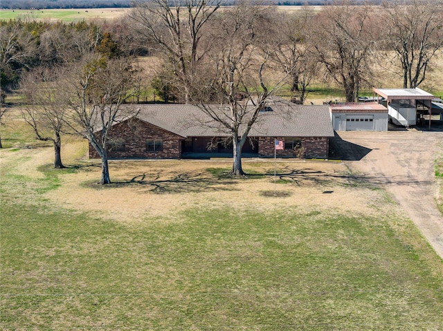 view of front of home with a front yard, brick siding, dirt driveway, and a rural view