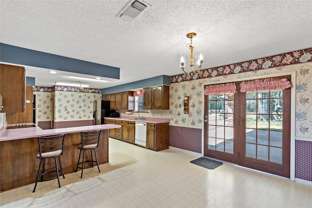 kitchen with light countertops, wainscoting, white dishwasher, and wallpapered walls