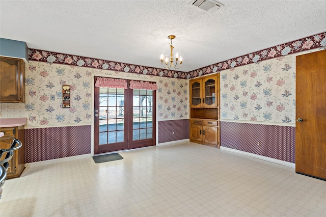 interior space featuring wallpapered walls, visible vents, wainscoting, a textured ceiling, and light floors