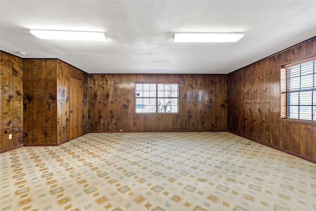 empty room with baseboards, wood walls, and light colored carpet