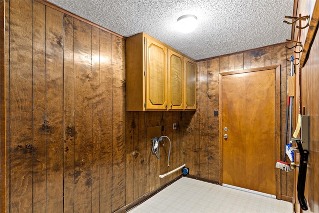 laundry room with cabinet space, wooden walls, light floors, and a textured ceiling