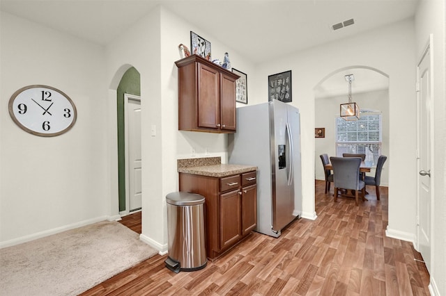 kitchen with arched walkways, visible vents, baseboards, stainless steel refrigerator with ice dispenser, and light wood finished floors