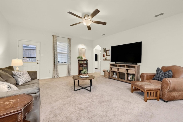 living area featuring arched walkways, light colored carpet, ceiling fan, and visible vents