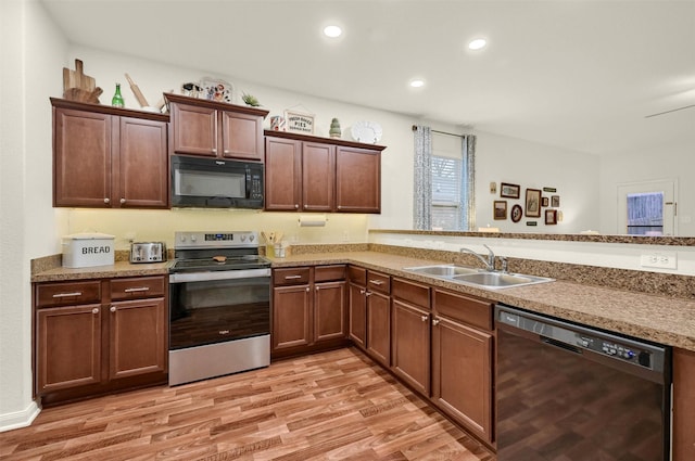 kitchen featuring a peninsula, light wood-type flooring, black appliances, a sink, and recessed lighting