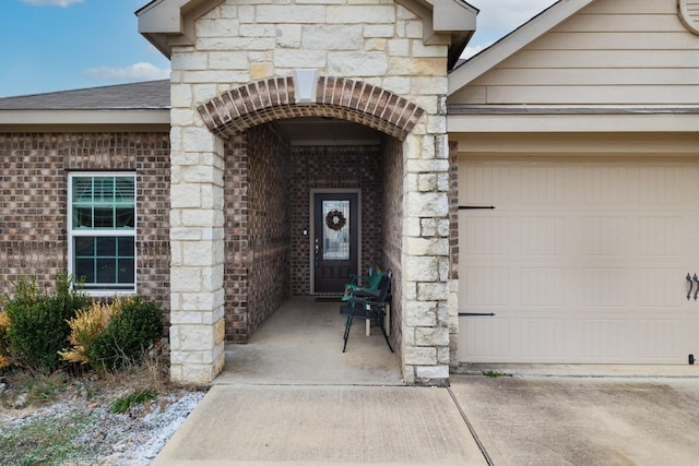 entrance to property with a garage, stone siding, brick siding, and a shingled roof