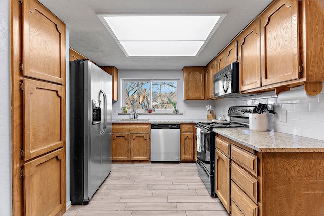 kitchen featuring decorative backsplash, brown cabinets, a sink, and black appliances