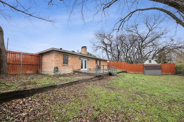 rear view of house featuring an outdoor structure, a fenced backyard, brick siding, a yard, and a chimney