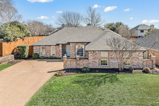 french country inspired facade featuring brick siding, a shingled roof, fence, concrete driveway, and a front yard