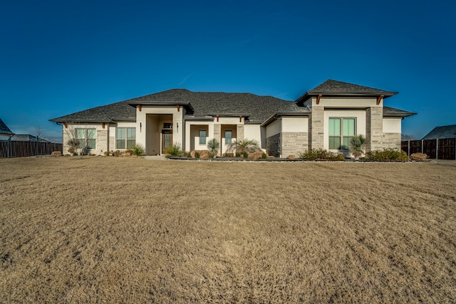 prairie-style home featuring stone siding, a front lawn, and fence