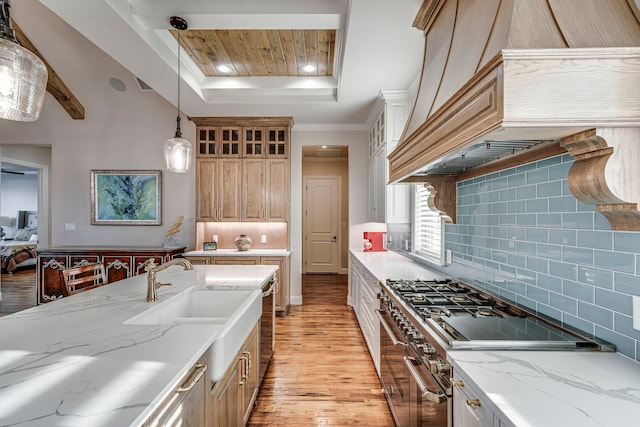 kitchen featuring range with two ovens, a tray ceiling, pendant lighting, light stone counters, and light wood-type flooring