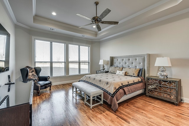 bedroom featuring light wood-style floors, visible vents, a tray ceiling, and ornamental molding