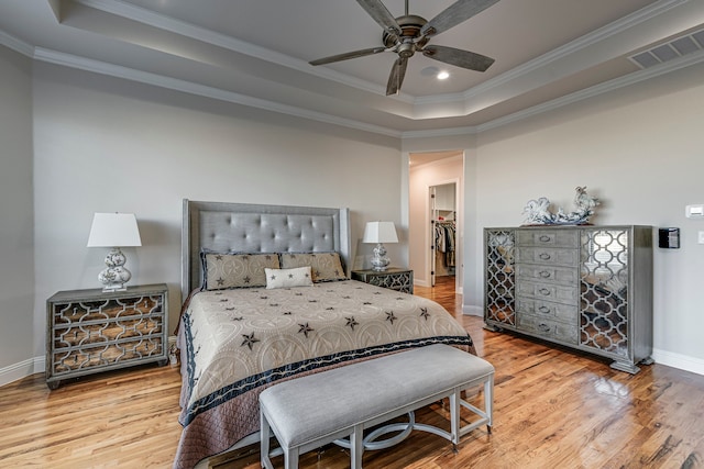 bedroom featuring wood finished floors, visible vents, baseboards, a raised ceiling, and crown molding