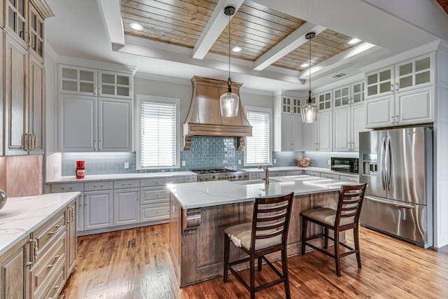 kitchen with a center island with sink, glass insert cabinets, stainless steel appliances, and a raised ceiling