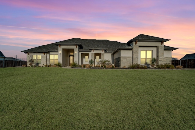 prairie-style house with stone siding, fence, and a front lawn