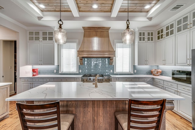 kitchen with custom exhaust hood, glass insert cabinets, white cabinets, and a large island with sink