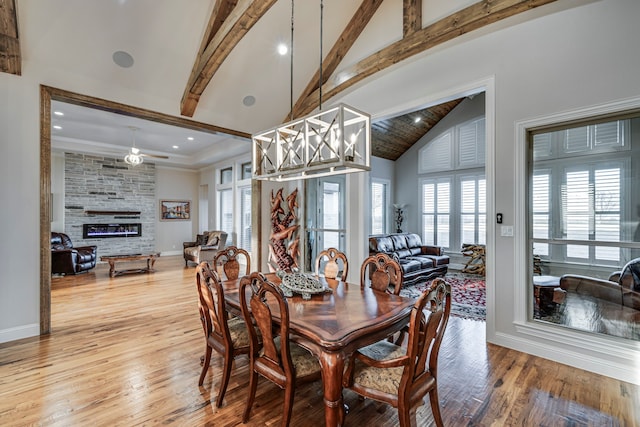 dining room with high vaulted ceiling, beam ceiling, a fireplace, and wood finished floors