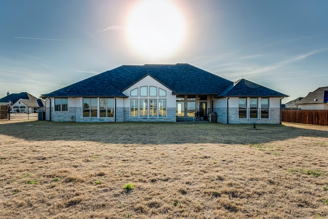 back of property featuring stone siding, fence, and a lawn